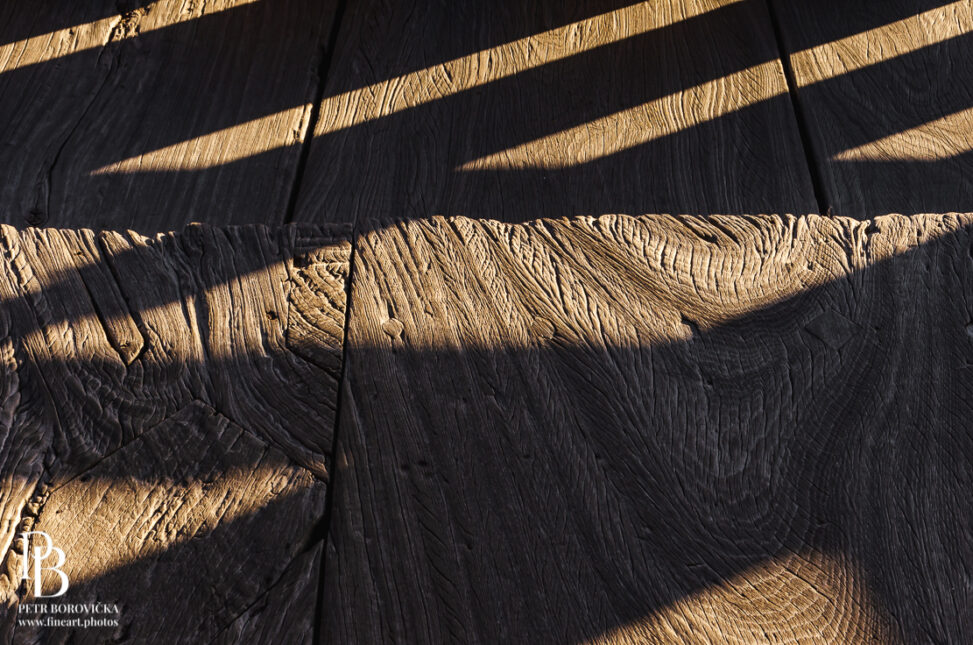 Warm sunlight and deep geometric shadows cast across the textured, 500-year-old wooden floorboards of Senjokaku hall in Miyajima.