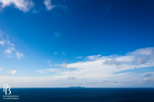 A solitary island surrounded by the vast, deep blue Pacific Ocean off the coast of Okinawa, framed with expansive negative space.