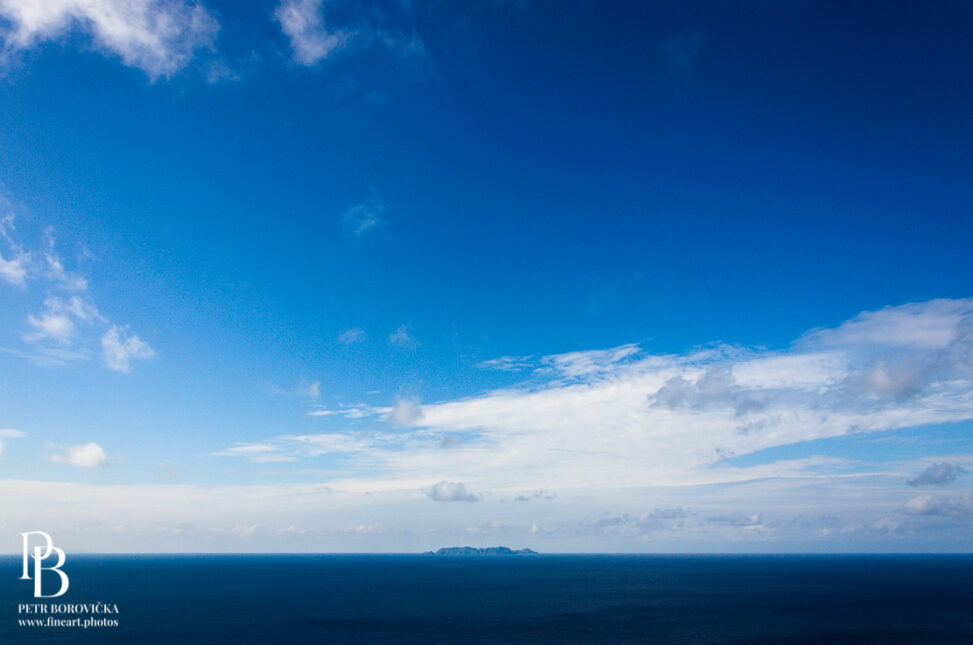 A solitary island surrounded by the vast, deep blue Pacific Ocean off the coast of Okinawa, framed with expansive negative space.